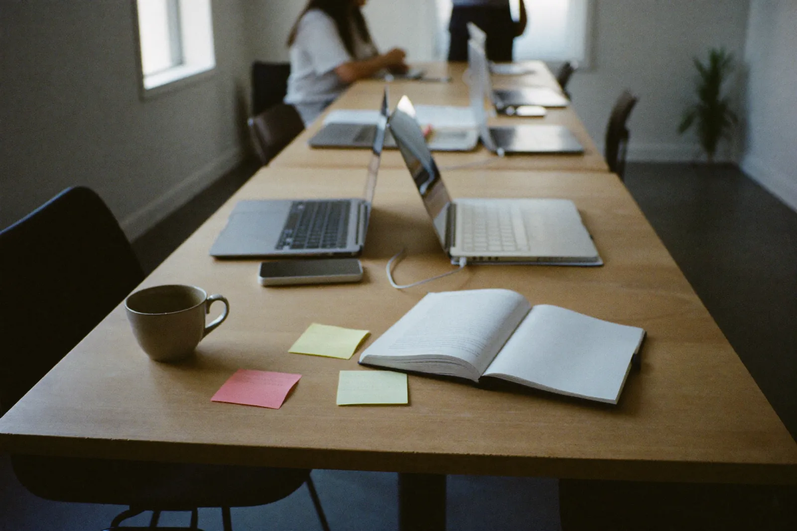 A long work table in a small agency office: open laptops, a cup of coffee, a notebook and blank sticky notes
